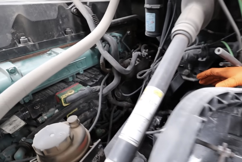 Technician working on diesel engine hoses and wiring under the hood